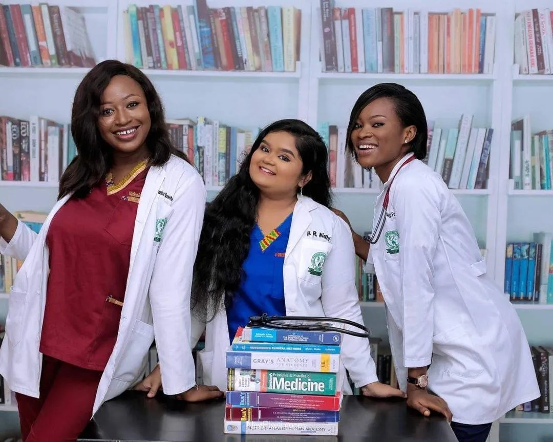 Three alumnae in white coats in front of a bookcase